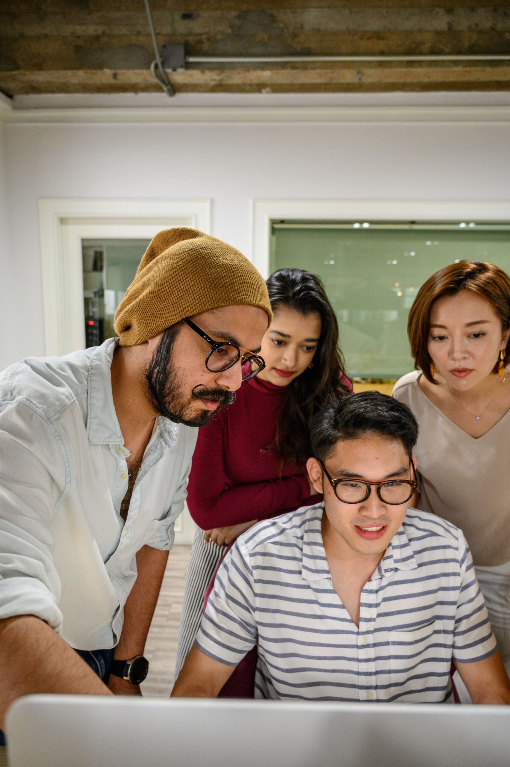 A diverse team collaborates around a computer in a contemporary office space.