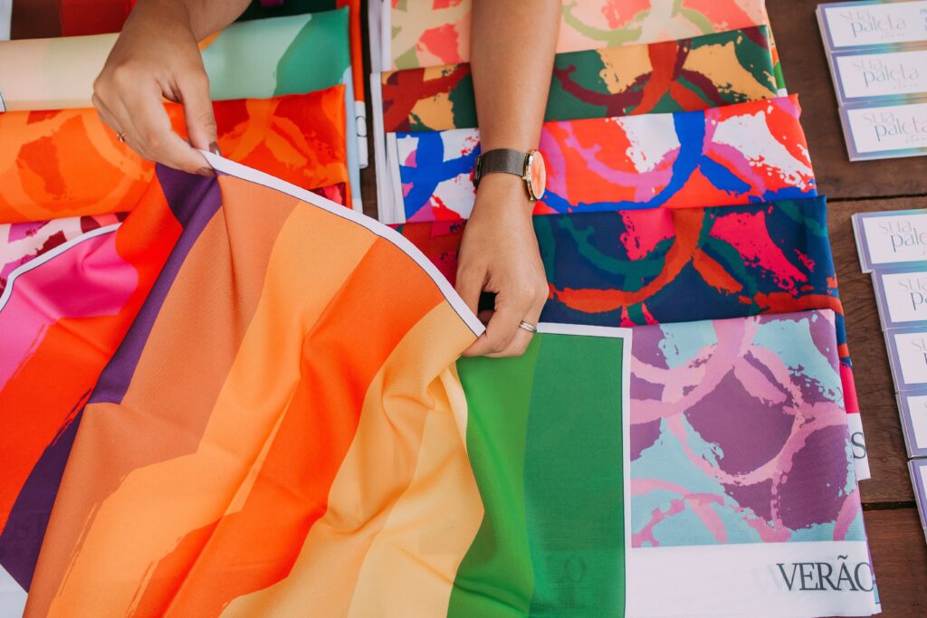 Close-up of hands handling vibrant fabric samples, showcasing diverse patterns and colors.