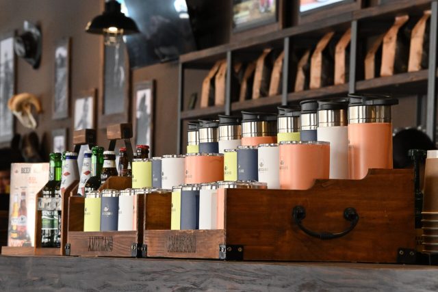 Modern coffee shop interior featuring assorted bottles and thermoses on a rustic wooden bar.