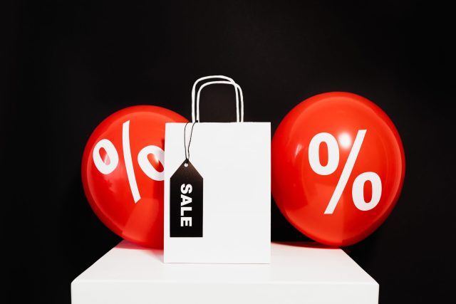 Shopping bag with sale tag and percentage balloons on black background.